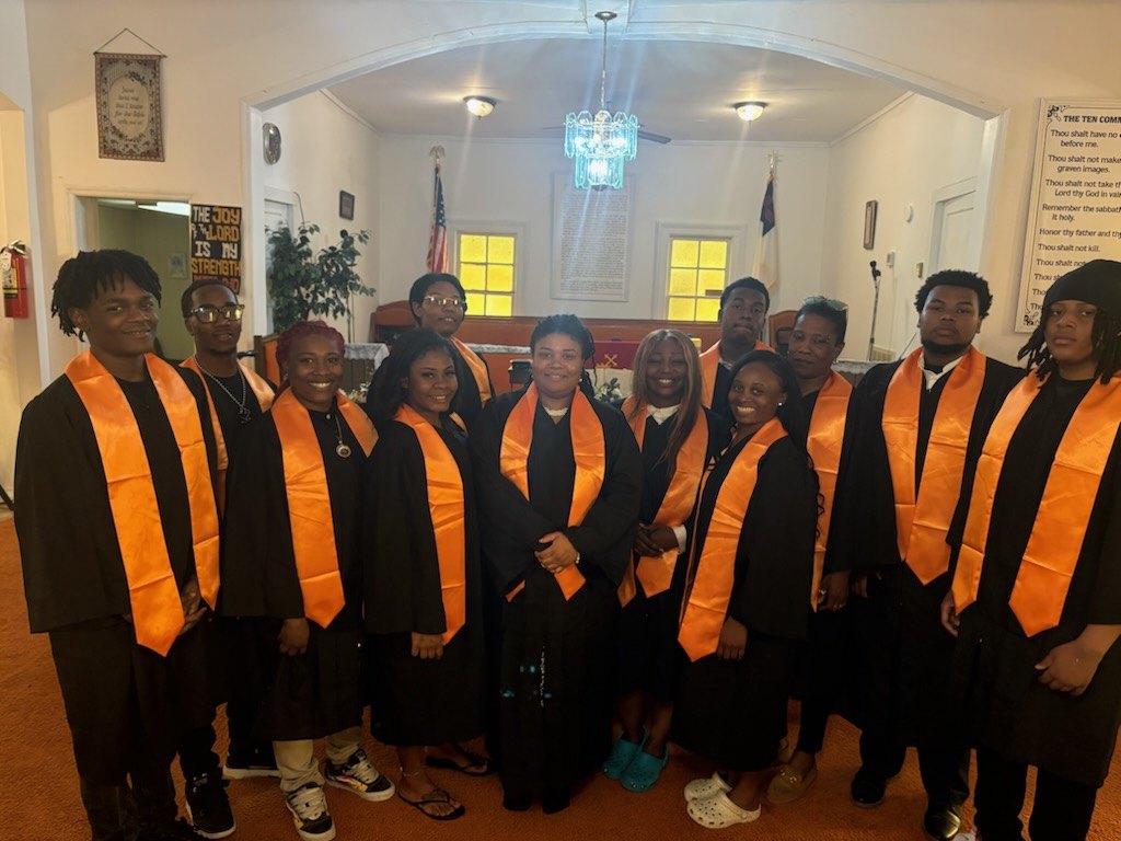 The youth choir in black robes and orange stoles, standing together in the sanctuary
